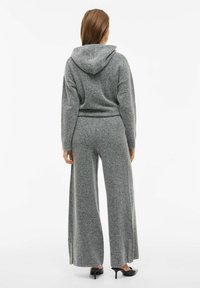 Szary zestaw dresowy z dzianiny, składający się z bluzy z kapturem i szerokich spodni, z ozdobnym sznurkiem w kapturze, luźnym krojem oraz rozcięciami na dolnej krawędzi spodni. Gładka tekstura.