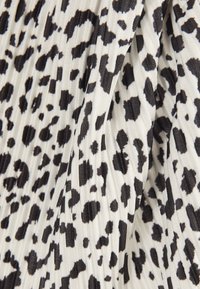 Czarno-biała tkanina plisowana z nieregularnymi, rozrzuconymi czarnymi plamami w wzór panterki.