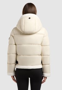 Cream puffer jacket with a plush fleece-lined hood, wide horizontal quilting, and black hardware accents. Finished with fleece trim at cuffs.