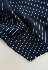 Tissu bleu marine à fines rayures blanches, présentant une texture douce et un coin replié, mettant en valeur des coutures nettes et des bords lisses.