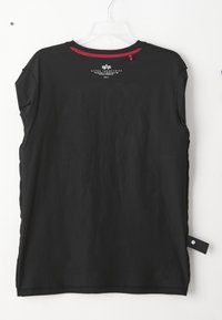 Sort Alpha Industries ærmeløs skjorte med rød inner halskant, hvidt logo og tekst på ryggen, hængende på en klar plastikbøjle.