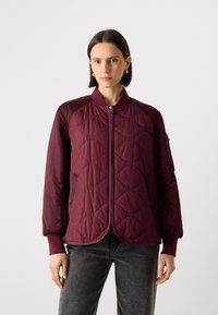 Giacca bomber trapuntata bordeaux con polsini a coste e scollatura rotonda. Presenta una zip frontale e un motivo a forma di diamante discreto.