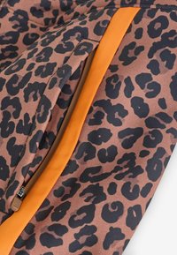 Tkanina w panterkę w odcieniach brązu i czerni, z pomarańczowym paskiem dekoracyjnym i kieszenią na zamek. Trwały, teksturowany materiał.