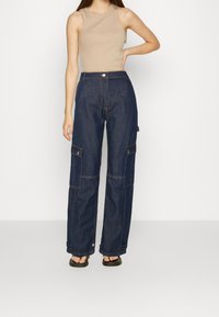 Mörkblå denim cargobyxor med vida ben, med två sidofickor och kontrasterande gul sömnad. Matchas med en beige ärmlös topp.