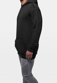 Sudadera negra hecha de un tejido suave, con un bolsillo tipo canguro, puños acanalados y detalles desgastados en las costuras.