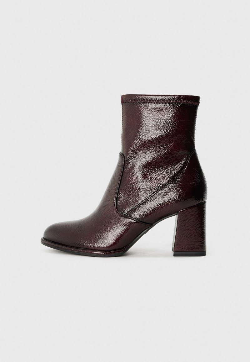 Bottine en cuir marron foncé avec talon carré, bout arrondi et détails de couture visibles sur un fond neutre.