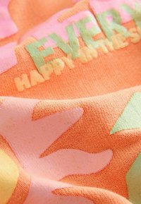 Textil con fondo naranja y formas abstractas de colores en rosa, amarillo y verde. Presencia de texto en colores mixtos.