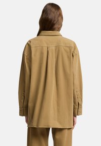 Khaki koszula oversize wykonana z miękkiego materiału. Posiada klasyczny kołnierzyk, guziki na mankietach oraz plisowane tylne wykończenie dla swobodnego dopasowania.