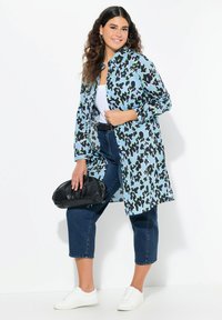 Cappotto a stampa floreale in azzurro chiaro con accenti neri e verdi, maniche lunghe, davanti aperto, abbinato a jeans in denim e sneakers bianche.