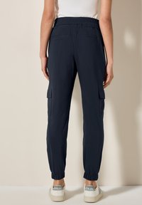 Marinenfärgade cargo-byxor med elastiskt midjeband, med sidofickor och elastiska manschetter vid anklarna. Tillverkade av lättviktsmaterial.