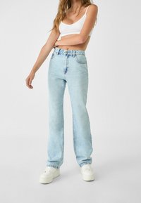 Vaqueros de mezclilla azul claro con cintura alta, corte recto y detalles desgastados sutiles. Combinados con zapatillas blancas.