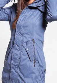 Mörkblå isolerad jacka med dragkedja fram, två snedställda ficklock och en texturerad tygbåge på fickorna. Sytt detaljer är synliga.