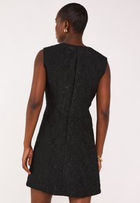 Schwarzes Kleid aus strukturiertem Stoff, ärmelloses Design und figurbetonter Silhouette. Verfügt über einen verdeckten Reißverschluss hinten und einen leichten Schwung am Saum.