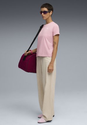 Roze katoen t-shirt met logo, beige wijde pantalons, roze sportieve schoenen, paarse zonnebril, en een magenta sporttas met zwarte accenten.
