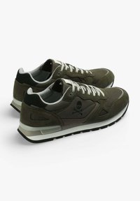Olivgrüne Sportschuhe aus Wildleder und Mesh-Materialien, mit schwarzen Akzenten, weißen Schnürsenkeln und einem Totenkopf-Logo an der Seite.