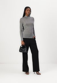 Un haut gris à manches longues avec col roulé associé à un pantalon noir à jambes larges. Le modèle tient un petit sac à main noir et porte des talons à lanières.