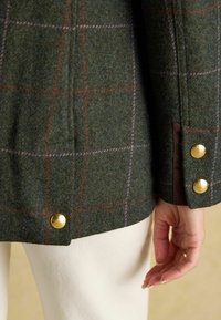 Giacca di lana a quadri verdi con bottoni dorati e una finitura texturizzata, con accenti rosa e rossi nel motivo. Vista dettagliata del maniche.