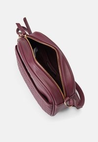 Burgundy läder crossbody-väska med en strukturerad sida, detalj med guldfärgad dragkedja och handtag upptill för enkel bärbarhet. Öppen, som visar ett inre fack.
