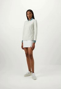 Pulôver de manga longa cinza claro com gola e detalhes em azul-piscina, combinado com uma mini saia branca e sapatilhas brancas.