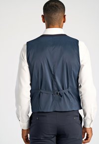 Marineblauer Weste aus glattem Stoff, mit einer Rückenbuckle und verstellbarem Riemen, getragen über einem weißen Hemd mit geknöpften Manschetten.