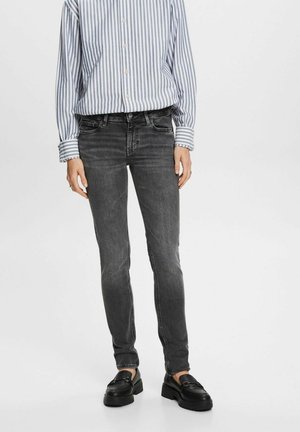 Persoon die zwarte slim-fit jeans, zwarte loafers en een wit met blauwe verticale gestreepte knoop-overhemd draagt.