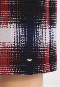 Jupe jusqu'aux genoux à motif à carreaux rouge, marine et blanc. Présente une texture lisse et une petite étiquette métallique sur l'ourlet.