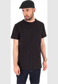 Black cotton t-shirt with a crew neck, short sleeves, paired with dark denim jeans and a black flat cap, featuring a smooth texture.