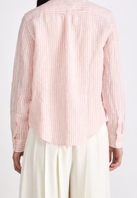 Lekka, różowo-biała w paski koszula z długim rękawem i zaokrąglonym dołem, wykonana z oddychającego materiału.