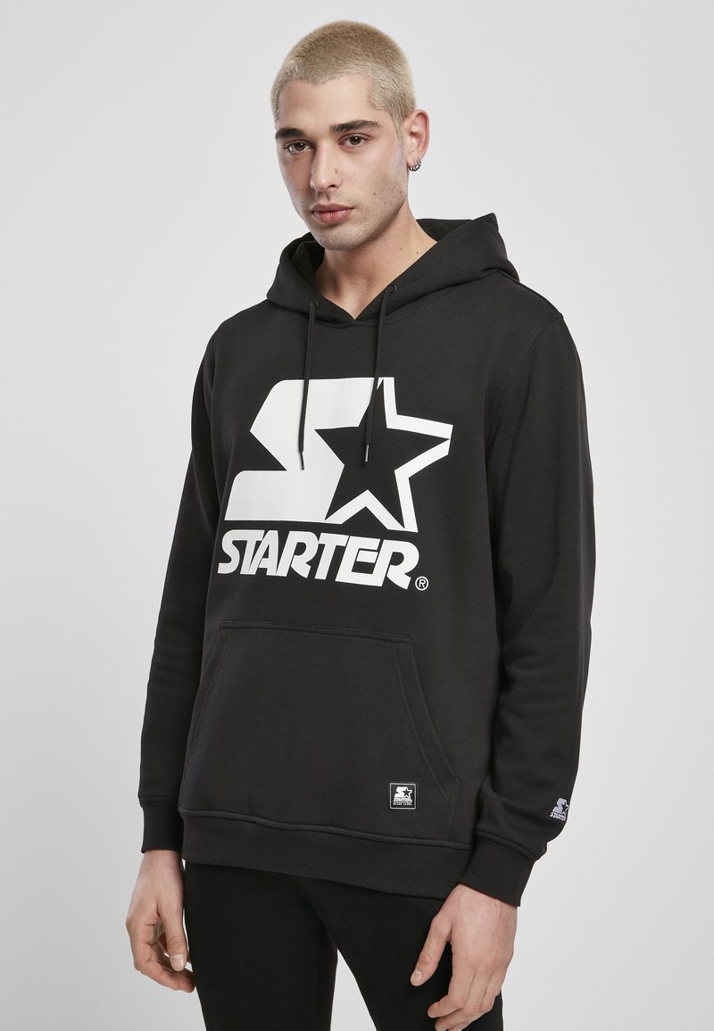 Svart hettegenser med en stor hvit "STARTER" logo og stjernedesign. Laget av et strukturert materiale med en lomme foran og snor i hetta.