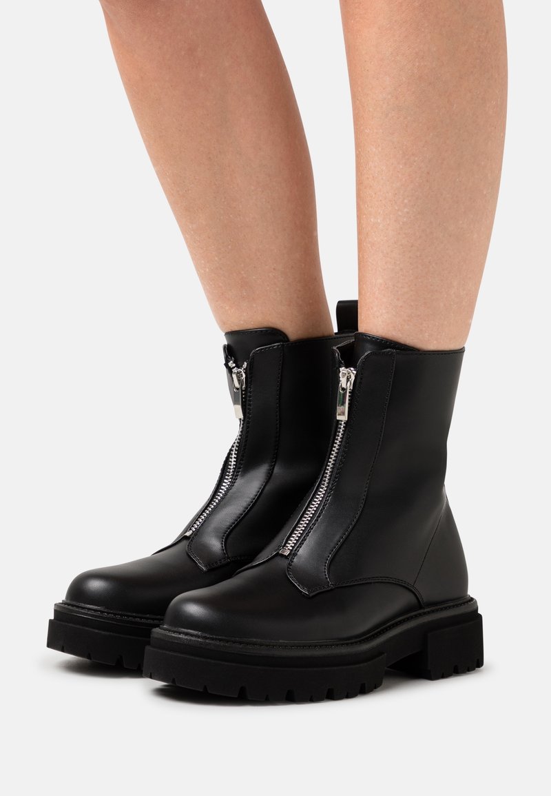 Botines negros hasta el tobillo con acabado en cuero liso, que presentan una cremallera diagonal y una suela gruesa para mayor agarre y estabilidad.