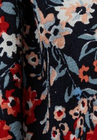 Tissu foncé avec motif floral texturé en rouge, beige, bleu et blanc, comportant des pétales et des feuilles en couches.