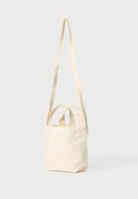 Kanvas tote-bag i lys kremfarge med to topper og en lang justerbar stropp. Enkelt design, myk tekstur og uformet form.