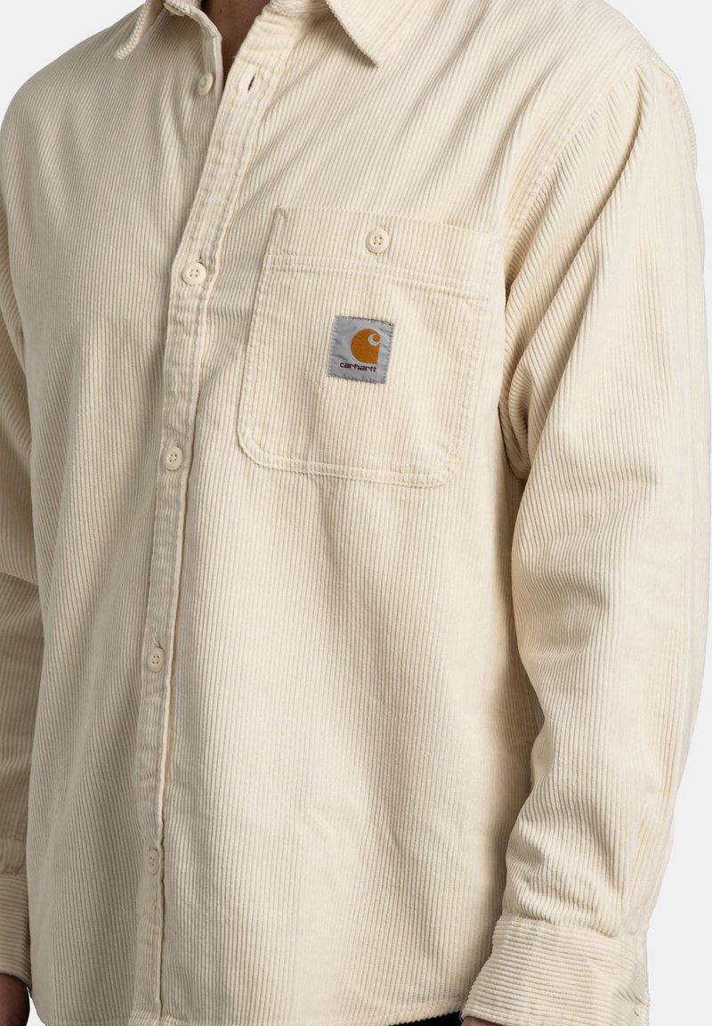 Cream-colored corduroy shirt with a button-up front, a chest pocket featuring a logo, and long sleeves with buttoned cuffs.