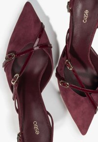 Burgundzkie szpilki z szpiczastym noskiem, wykonane z zamszu i lakierowanej skóry. Posiadają krzyżujące się paski i akcenty w kolorze złotym.