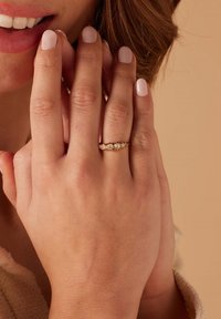 Gouden ring met drie heldere stenen, gezet op een delicaat bandje. De hand heeft een zachte huid met een lichte nagellak. Eenvoudig en elegant ontwerp.