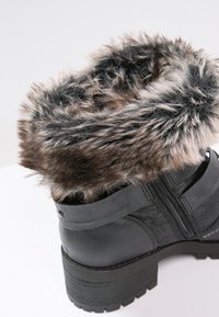 Černá kožená kotníková bota s límcem z umělé kožešiny, texturovaným povrchem, pevným podešví a bočním zipem. Obsahuje robustní blokový podpatek.