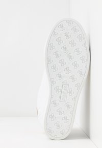 White sneaker featuring a textured white sole with a repeated embossed logo pattern and a brand label at the midsole.
