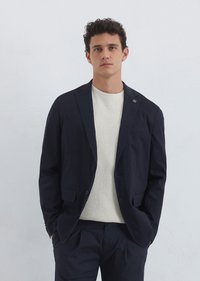 Navy blazer with two front pockets and a single button closure, worn over a light textured knit sweater. Smooth fabric, modern fit.