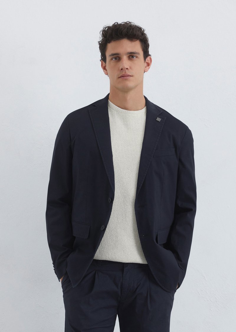 Navy blazer with two front pockets and a single button closure, worn over a light textured knit sweater. Smooth fabric, modern fit.