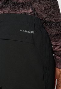 Zwarte outdoorbroeken met een slank ontwerp, rekbare stof en een zijzak. Het merk "Mammut" staat in het grijs op de tailleband.