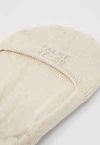 Chaussette beige mi-mollet en tissu doux et texturé, avec une couture élastique lisse en haut et un logo discret imprimé près de la cheville.
