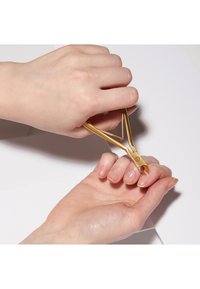 Dłoń używająca złotych cążek do manicure do obcinania skórek na paznokciach nad białą powierzchnią.