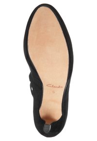 Černá nubuková bota s otevřeným designem, obsahující hladkou koženou vložku a tištěné jméno značky. Podešev je béžová s jemnými drážkami.