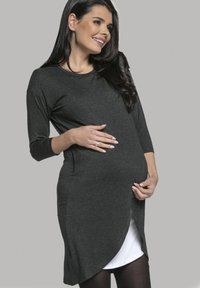 Schwangerschaftskleid aus dunkelgrauem Jersey-Stoff mit Dreiviertelärmeln, geschwungenem Saum und weißem Futter, das am Boden sichtbar ist.