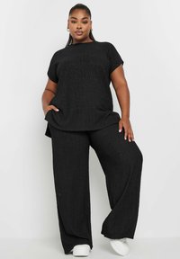 Czarny dwuczęściowy zestaw składający się z teksturowanej, krótkosłej koszulki oraz spodni z szerokimi nogawkami, wykonany z lekkiego materiału. Uzupełniony białymi trampkami.