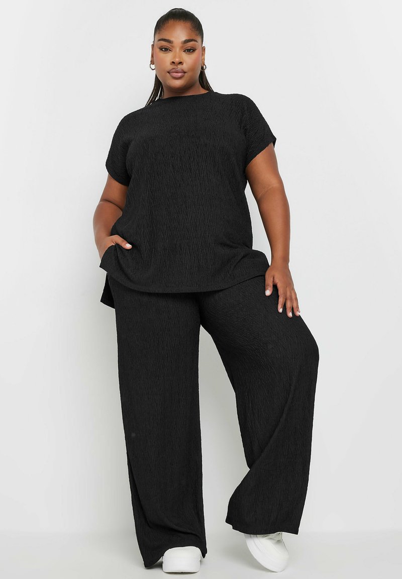 Czarny dwuczęściowy zestaw składający się z teksturowanej, krótkosłej koszulki oraz spodni z szerokimi nogawkami, wykonany z lekkiego materiału. Uzupełniony białymi trampkami.