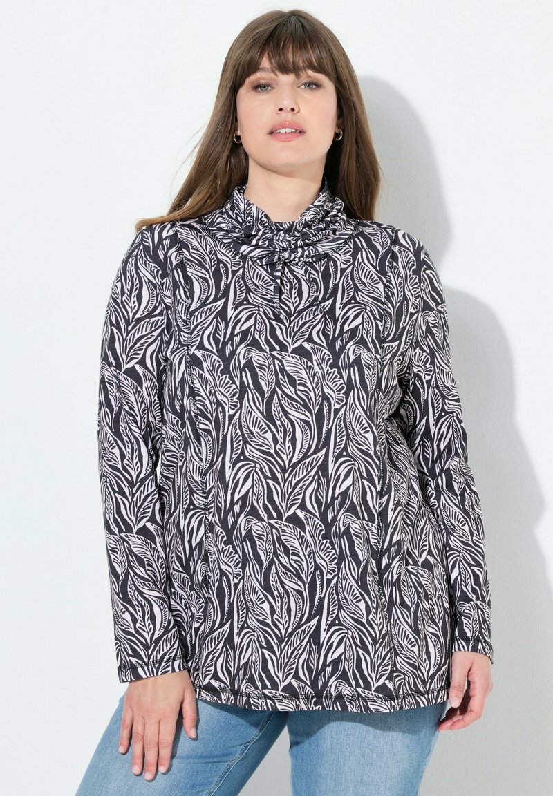 Haut à manches longues avec un col drapé, en tissu noir orné de motifs de feuilles blanches. Accompagné de jeans en denim bleu clair.