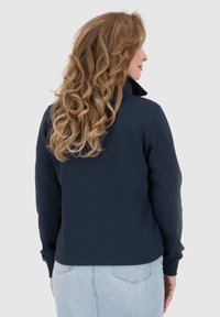 Felpa navy blue con colletto alto, maniche lunghe e polsini a coste. Tessuto morbido con una finitura liscia, presenta un taglio aderente in vita.