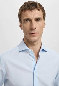 Lekka, niebieska koszula na guziki o miękkiej fakturze, klasycznym kołnierzu i delikatnym połysku. Koszula jest starannie dopasowana, prezentując czysty design.