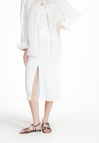 Gonna midi bianca in cotone con spacco frontale, abbinata a una camicia button-up beige a righe e sandali neri con cinturini. Tessuto morbido e design casual.